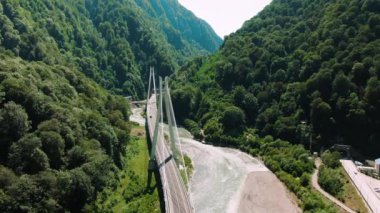 Havadan 4k görünüm. Nehir üzerinde asma köprü. Dağlar ve kayalar arasında köprü üzerinde uçan.