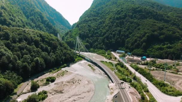 Havadan 4k görünüm. Nehir üzerinde asma köprü. Dağlar ve kayalar arasında köprü üzerinde uçan. — Stok video