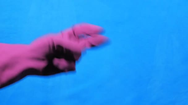 Чиста рука в фіолетовій гумовій рукавичці на синьому фоні. Скеля, папір, ножиці . — стокове відео