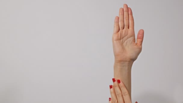 Parlak kırmızı manikür ile güzel genç kadın elleri, bir el yavaşça diğer masaj, gri arka plan üzerinde izole — Stok video