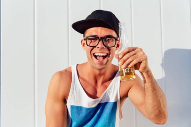 Komik adam kamera bakarken bir şişe bira tutar, açık havada