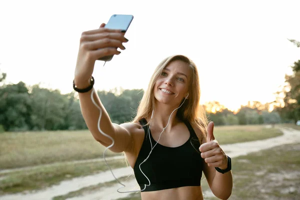 Sonriente chica deportiva mostrando un pulgar hacia arriba mientras toma una selfie al aire libre — Foto de Stock
