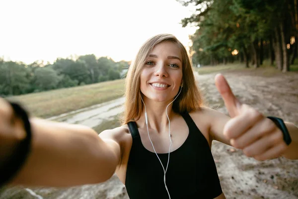 Chica alegre mostrando un pulgar hacia arriba mientras se toma una selfie, al aire libre — Foto de Stock