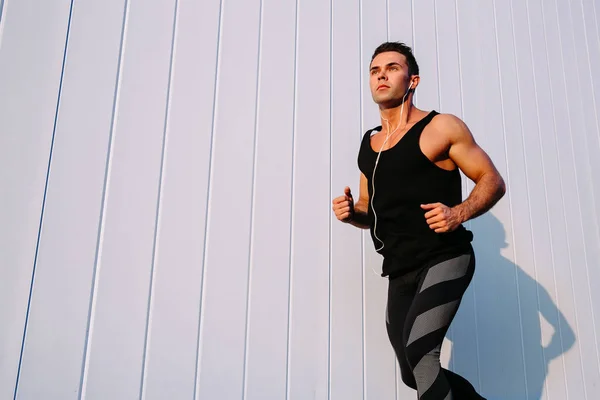 Hombre musculoso corriendo contra la pared blanca, al aire libre — Foto de Stock