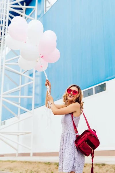 Chica divertida posando en la cámara mientras sostiene globos de aire, afuera . — Foto de Stock