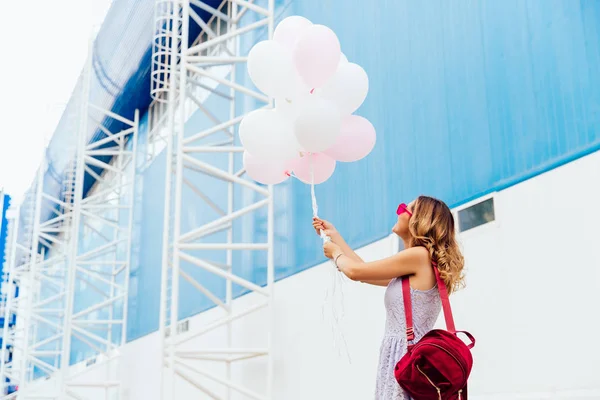 Trendy kız her iki eliyle hava balonları tutar, açık havada.