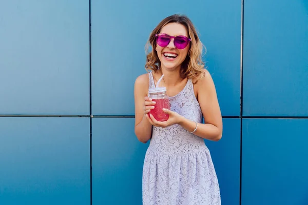 Chica alegre en gafas de sol tiene bebida de frutas, divertirse al aire libre — Foto de Stock