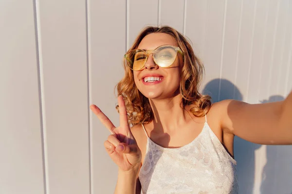 Muchacha atractiva mostrando un signo de paz mientras se toma una selfie, al aire libre — Foto de Stock