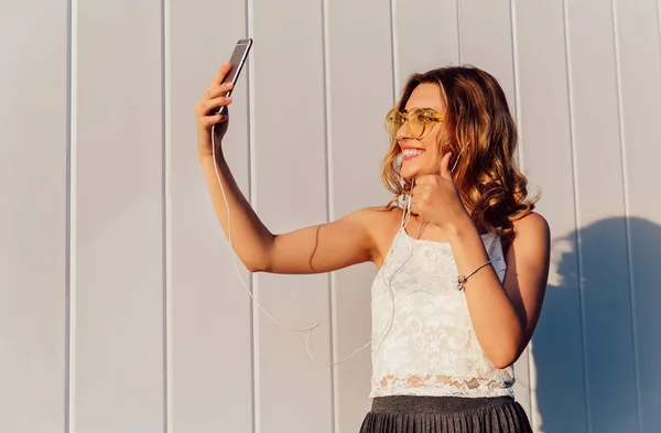 Szczęśliwy dziewczyna pokazując kciuk w górę podczas robienia selfie na telefon komórkowy — Zdjęcie stockowe