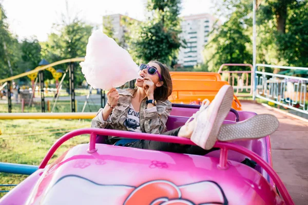 Hermosa chica comiendo un algodón de azúcar, disfrutando del día soleado en el parque de atracciones — Foto de Stock