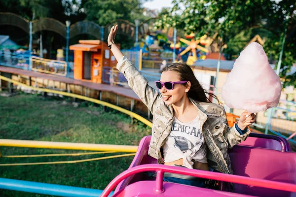 Chica emocionada con algodón de azúcar montando una montaña rusa para niños — Foto de Stock