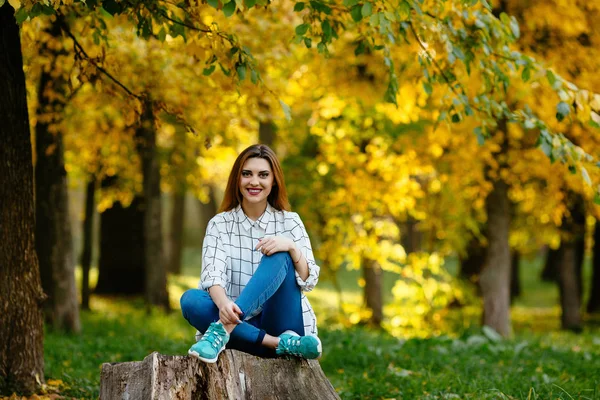 Šťastné ženy sedí na pahýlu s pozadím podzimních barevných stromů. — Stock fotografie