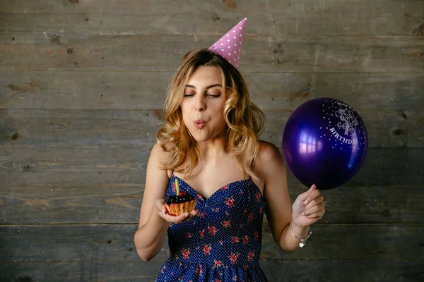 Pretty girl blowing out the candle on cupcake and holds the ball — Stock Photo, Image