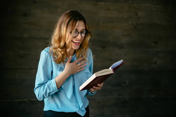 Mujer atractiva riendo después de leer una broma divertida en el libro . —  Fotos de Stock