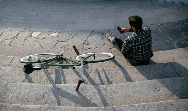 Вид зверху на молодого чоловіка зі смартфоном, сидячи на сходах біля велосипеда — стокове фото