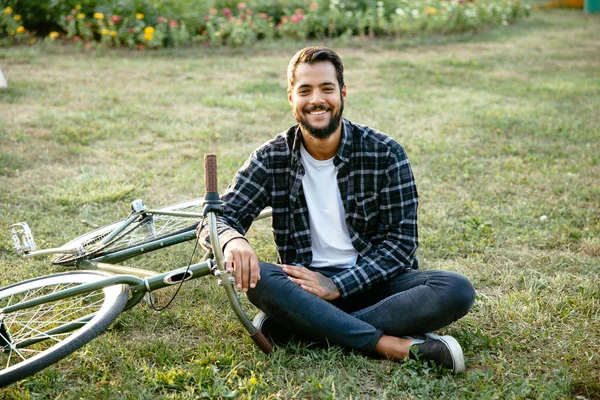 Glücklicher Mann sitzt mit Fahrrad auf Gras im Park — Stockfoto