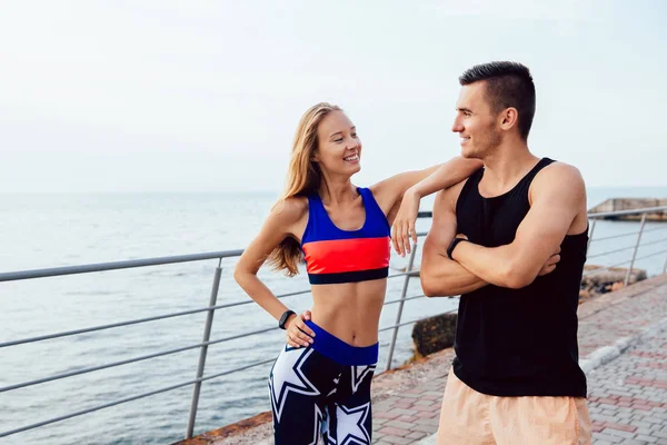 Pareja joven en ropa deportiva de pie en el muelle cerca del mar . — Foto de Stock