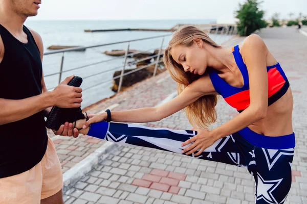 Joven ayuda a una chica a estirar su cuerpo al aire libre — Foto de Stock
