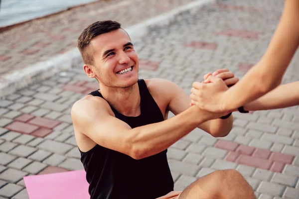 Mujer persona ayuda a un deportista a levantarse, al aire libre — Foto de Stock