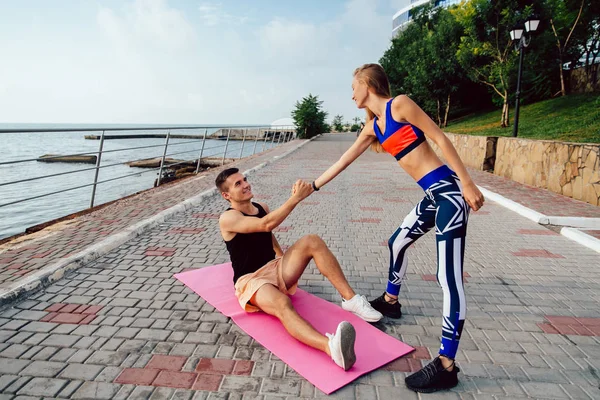 Chica joven ayuda a un deportista a levantarse, durante el entrenamiento al aire libre — Foto de Stock