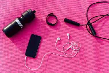Kulaklıklı cep telefonu, saatler, ip atlama ve su şişesi pembe arka planda