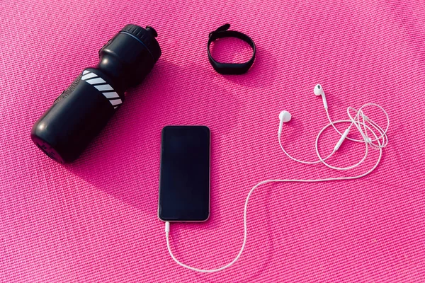 Smartphone with headphones, watches and bottle of water are on pink background