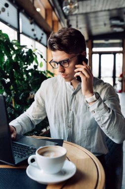 Düşünceli işadamı dizüstü bilgisayar ile kafede otururken akıllı telefon konuşuyor