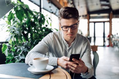 Kulaklık düşünceli adam, cep telefonu bakarak, bir dinlenme