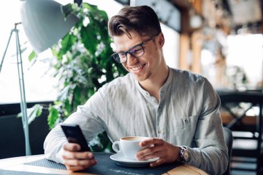 Kafede dinlenirken akıllı telefon ekranına bakan gülümseyen adam