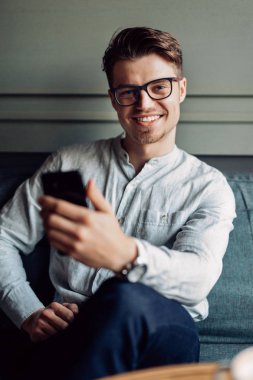 Kafede akıllı telefonu tutan gözlüklü gülümseyen adam