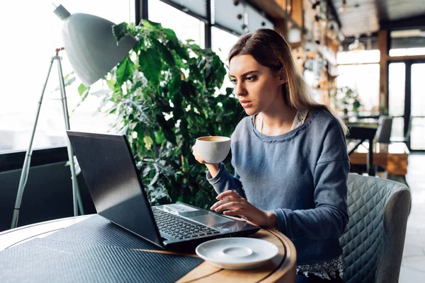 Piękna kobieta picie kawy w kawiarni podczas pracy na laptopie — Zdjęcie stockowe
