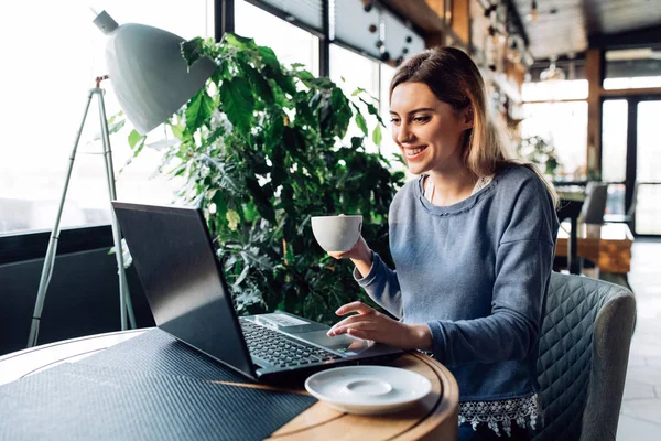 Chica sonriente sentada en el café con el ordenador portátil — Foto de Stock