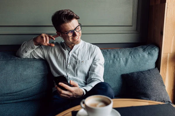 Hombre sonriente escuchando música en los auriculares mientras toma un descanso en la cafetería — Foto de Stock