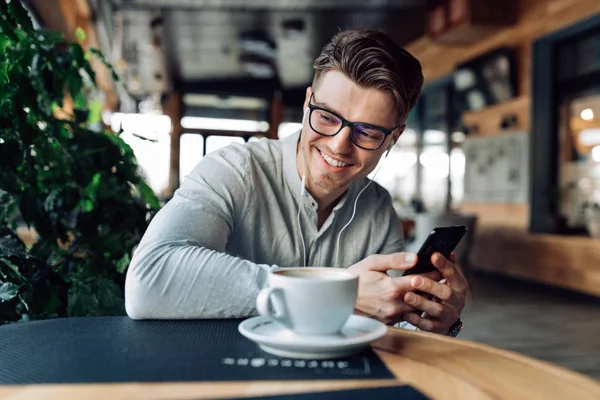 Happy guy listening to music in earphones, spending time at cafe