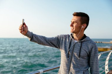 Neşeli adam akıllı telefonda, denize yakın selfie çekiyor