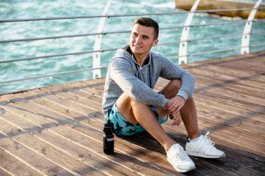 Kulaklık neşeli adam, egzersiz sonrası dinlenme, iskelede, deniz.