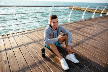 Cep telefonu kullanan, iskelede, deniz de oturan yakışıklı adam