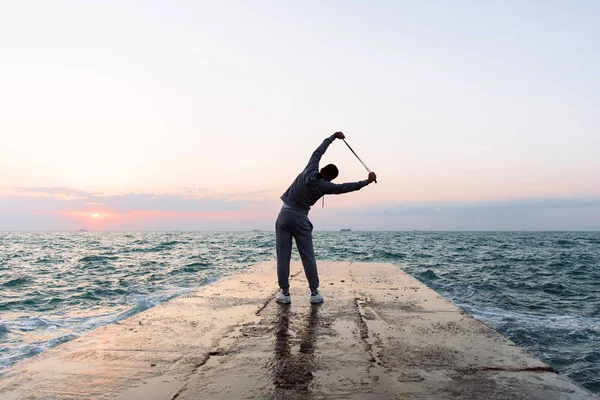 Foto completa del deportista que se estira con la cuerda que salta, cerca del mar — Foto de Stock