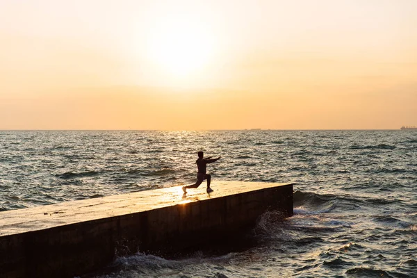 Vista desde lejos en deportista haciendo ejercicios para las piernas, en el muelle . — Foto de Stock