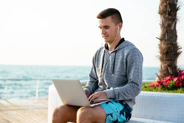 Sportive człowiek za pomocą laptopa, siedząc na ławce, nad morzem — Zdjęcie stockowe