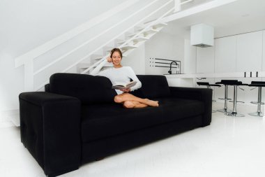 Güzel kadın kitap okuyor, evde kanepede oturuyor.