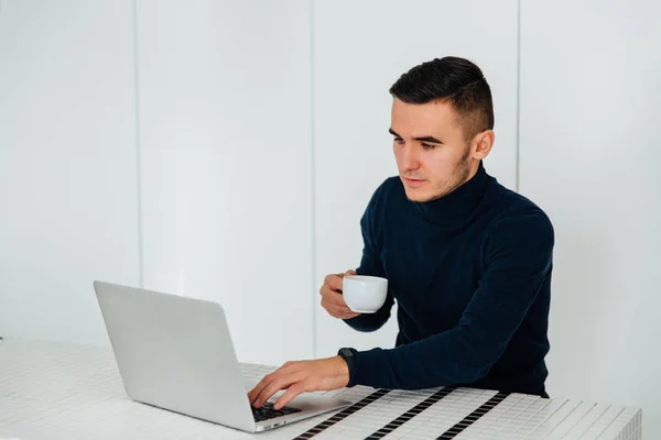 Hombre guapo usando un portátil y sostiene una taza de té — Foto de Stock
