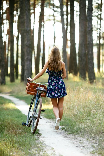 Girl goes on a bicycle path in the woods . Back view.