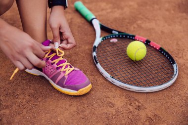 Sportif bir kadın tenis oynamaya hazırlanıyor, ayakkabı bağcıklarını bağlıyor. Yakın çekim görünüm.