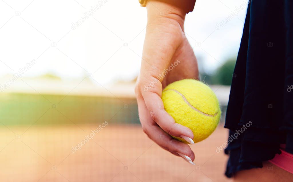 Woman holding tennis ball standing on the court. Close-up view.