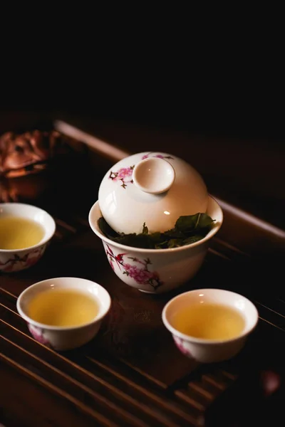 Chinese tea ceremony. Porcelain gaiwan, three cups of Chinese tea and golden frog on tea desk. Soft selective focus.