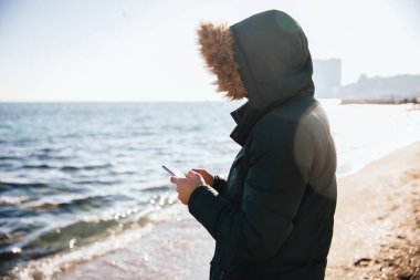 Sahilde dururken cep telefonu kullanan adam