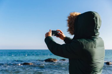 Deniz manzarasının fotoğrafını çeken adam