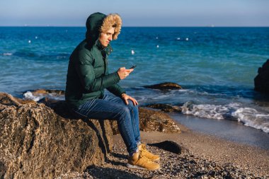 Yakışıklı adam deniz tarafından akıllı telefon kullanarak.