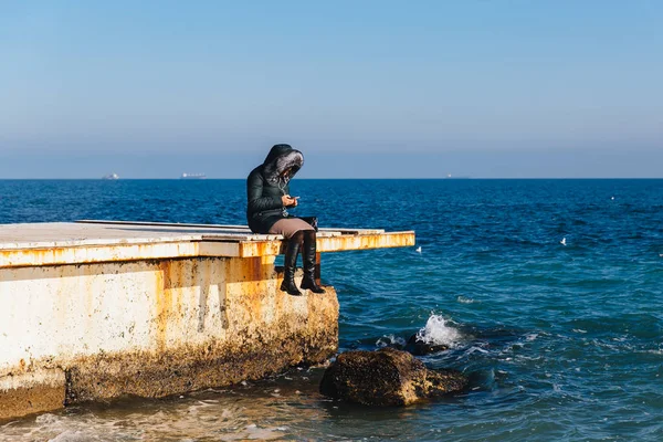 Mujer sentada en el muelle y usando un teléfono celular cerca del mar — Foto de Stock